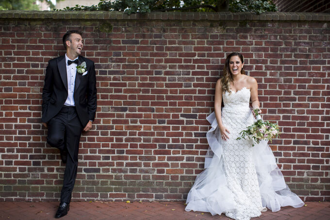 Bride and groom laughing against a brick wall